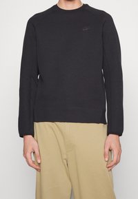 Svart sweatshirt med rund halsringning och långa ärmar, prydd med en liten svart Nike-logotyp på bröstet. Slät tyg och avslappnad passform.