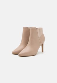 Stivali ankle in pelle beige con punta affusolata, tacco stiletto sottile e pannelli laterali elastici. Texture liscia con dettagli di cucitura minimi.