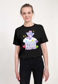 Camiseta negra con un gráfico colorido de los Care Bears, que presenta un oso morado sobre nubes y corazones. El diseño incluye el texto "Care Bears Forever".