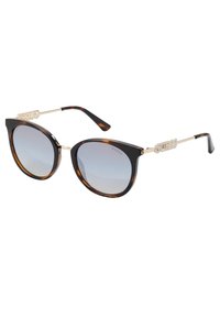 Occhiali da sole a forma di occhio di gatto in tartaruga con lenti sfumate, finiture in tonalità oro e accenti con il logo "GUESS" sulle stanghette. Design elegante.
