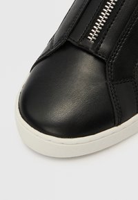 Czarny skórzany sneaker z zaokrąglonym noskiem, gładką fakturą i białą gumową podeszwą. Posiada srebrny suwak wzdłuż boku.