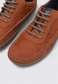 Chaussures en cuir marron avec une finition lisse, présentant des coutures blanches contrastées, un bout rond et des lacets beiges dans un design décontracté.