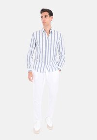 Camicia a maniche lunghe a righe in blu e bianco, con colletto button-down, abbinata a pantaloni bianchi in lino e sneakers bianche.