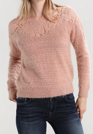 Maglione rosa chiaro con inserto in pizzo, texture morbida e pelosa, maniche lunghe e polsini a coste, abbinato a jeans blu scuro.
