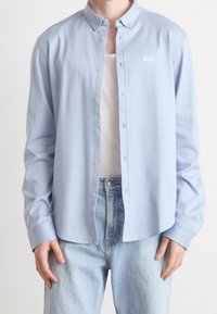 Hellblaues Hemd aus glattem Stoff mit klassischem Kragen und weißem „BOSS“-Logo, das auf der linken Brust gestickt ist.