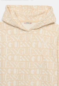 Beige hoodie featuring an all-over repeating "GUESS" logo pattern. Soft fabric with a kangaroo pocket and a drawstring hood.