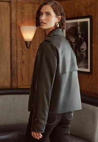 Chaqueta de cuero negro con un corte relajado, que presenta un diseño suelto en la parte posterior, puños abotonados y detalles de costura sutiles.