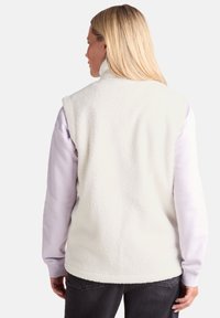 White fleece vest with high collar, soft texture, and sleeveless design, layered over a long-sleeve lavender top.