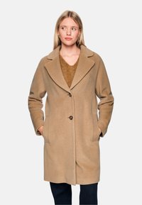 Beige Wollmantel mit Reverskragen, vorderer Knopfleiste und seitlichen Taschen. Weiche Textur und knielanges Design.