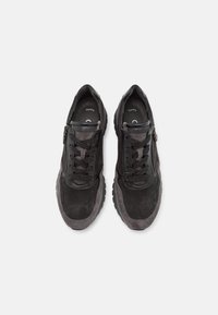Paire de baskets noires et gris foncé à lacets avec fermetures éclair latérales, vues de dessus sur un fond clair uni.