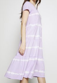 Lila bomullsklänning med V-ringning, korta ärmar, lagerdesign och vita tie-dye ränder. Faller strax under knäet.