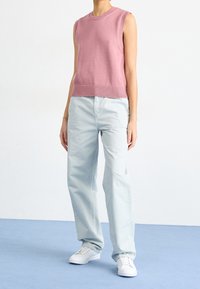 Sleeveless pink knit top with ribbed hem paired with light blue loose-fit pants and white sneakers, set against a plain background.