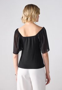 Top negru cu decolteu pătrat și mâneci umflate, transparente; textură netedă cu un corset ajustat și drapaj moale în spate.