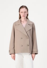 Beige dvouřadý kabát s velkými klopami, dvěma předními kapsami, zapínáním na patentky a širokými manžetami, v kombinaci se světlým topem.