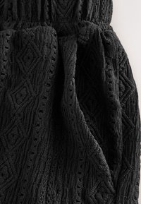 Black textured fabric with a diamond pattern and gathered waistband. Material appears soft with a slightly raised surface.