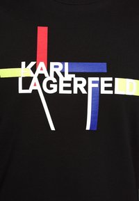Fond noir avec le texte blanc « KARL LAGERFELD » surmonté de lignes géométriques jaunes, rouges et bleues qui s'entrecroisent.