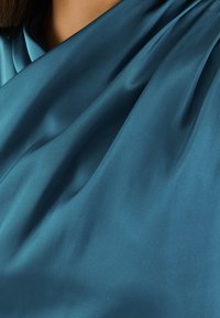 Tissu en satin bleu sarcelle avec une texture lisse, présentant un drapé doux et des plis subtils, mettant en valeur son design fluide et fluide.