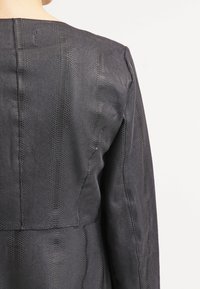 Giacca in pelle nera con texture, con motivo pitone, dotata di un collo semplice e una vestibilità aderente, cuciture visibili lungo le cuciture.