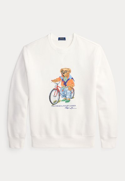 Weißes Sweatshirt mit langen Ärmeln, das einen Bären zeigt, der Sonnenbrillen trägt, eine orangefarbene Jacke, Jeans und grüne Schuhe anhat und neben einem roten Fahrrad steht.