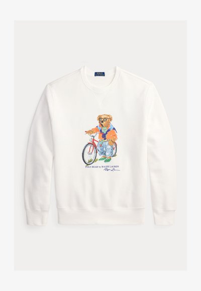 Weißes Sweatshirt mit langen Ärmeln, das einen Bären zeigt, der Sonnenbrillen trägt, eine orangefarbene Jacke, Jeans und grüne Schuhe anhat und neben einem roten Fahrrad steht.