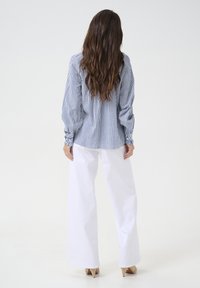 Blouse rayée à manches longues bouffantes en bleu et blanc, assortie à un pantalon large taille haute blanc et des talons beiges.