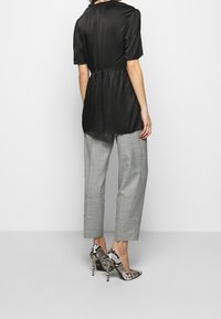 Top de satén negro con mangas cortas abullonadas, cintura ajustada, combinado con pantalones gris claro y zapatos de tacón alto con estampado.