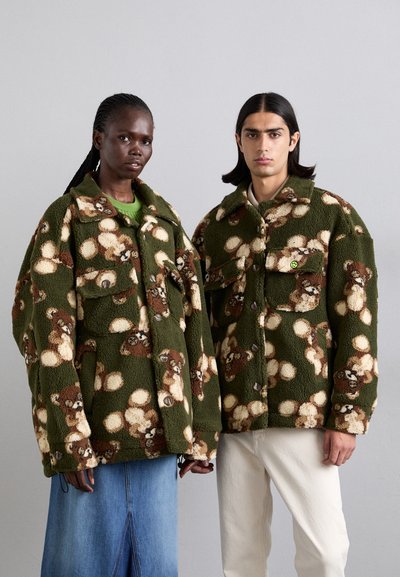 Fleece bundy v zelené barvě s hnědým a krémovým vzorem medvídků. Jsou vybaveny zapínáním na knoflíky a dvěma předními kapsami. Model má volný oversized střih.