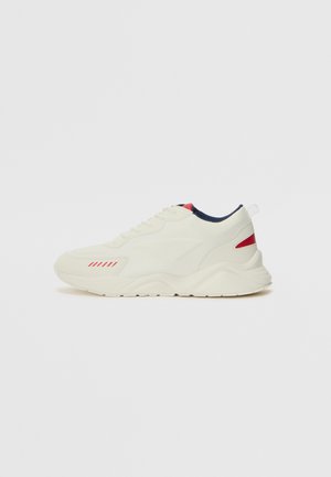 Sneaker in cream with textured leather and mesh, featuring red and navy accents. Rounded toe, lace-up design, and a thick rubber sole.