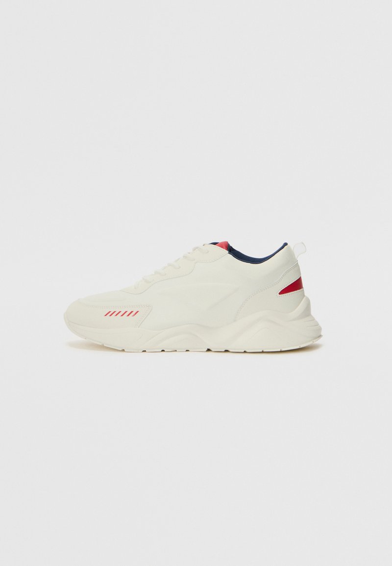 Sneaker in cream with textured leather and mesh, featuring red and navy accents. Rounded toe, lace-up design, and a thick rubber sole.