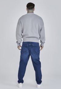 Hanorac gri cu umeri căzuți, manșete și talie ribbate, asociat cu blugi albaștri din denim, cu buzunare la spate și un croi lejer.