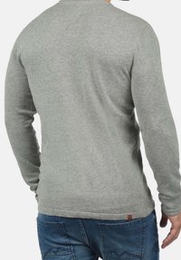 Grauer Pullover mit langen Ärmeln aus Strickstoff, mit rundem Ausschnitt, dezenter Textur und einem kleinen Markenetikett am Saum auf der Rückseite.