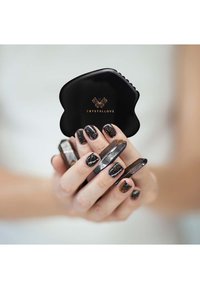 Fermaglio per capelli nero con design smerlato e logo dorato, tenuto tra le dita con unghie lunghe nere scintillanti, che mostra un'estetica di accessori moderna.