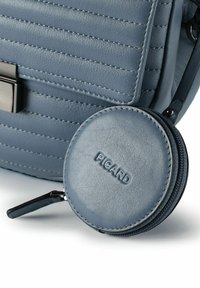 Borsa in pelle blu con cuciture verticali, dotata di tasca rotonda per monete con la scritta "PICARD" in rilievo e una cerniera nera.