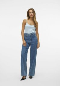 Lys blå tanktop med tynde stropper, udstyret med en lille sløjfe, parret med høj-til-maven, vide blå jeans og sorte spidse høje hæle.