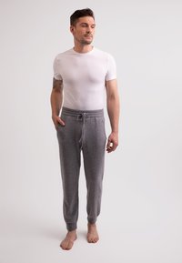 Graue Fleece-Jogginghosen mit elastischem Taillenbund und Kordelzug, ausgestattet mit Seitentaschen. Getragen mit einem engen, weißen T-Shirt mit kurzen Ärmeln.