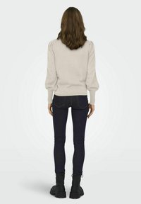 Suéter de punto gris claro con mangas abullonadas y detalles de calado, combinado con jeans ajustados azul oscuro y botas negras de tobillo, visto desde atrás.