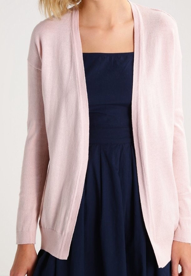 Ljusrosa stickad cardigan med långa ärmar, öppen front och ribbade muddar, bärs över en mörkblå klänning. Mjuk textur, klassisk design.