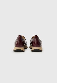 Burgundy patent leather shoes with a low heel, featuring a smooth texture and a contrasting beige sole. Rounded toe design with minimal detailing.