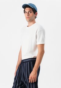 Biele krátke rukávy tričko skombinované s námorníckymi pásikavými nohavicami. Svetlomodrá čiapka dopĺňa outfit. Hladká textúra, pohodlný dizajn.