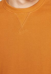 Sudadera naranja con un patrón de tejido texturizado, cuello redondo y costuras reforzadas en los hombros y el cuello.