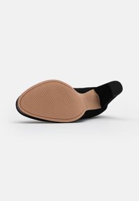 Chaussure en daim noir avec une semelle flexible, dotée d'une semelle extérieure en caoutchouc beige et d'une tige lisse et texturée. Conçue avec un bout pointu.