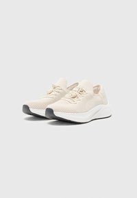 Chaussures de sport crème clair en tissu tricoté texturé, avec une semelle intermédiaire blanche et une semelle en caoutchouc grise, dotées d'un système de laçage.