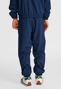 Mörkblå joggers med elastisk midja och muddar, gjorda av ett slätt material. Bärs med vita och gröna sneakers.