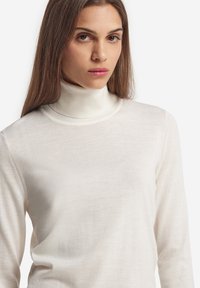 Leichter, cremefarbener Rollkragenpullover aus weichem Stoff, mit langen Ärmeln und taillierter Passform. Strukturstrick mit dezenten Nähten.