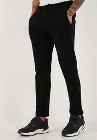 Schwarze Jogginghosen aus weichem Stoff. Mit elastischem Bund, seitlichen Taschen und schmal zulaufenden Beinen. Kombiniert mit schwarzen Sportschuhen.