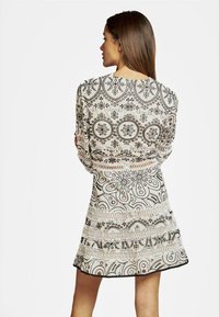 Vestido blanco con patrones florales negros, mangas transparentes y un dobladillo de encaje. La parte posterior presenta un escote redondo y un detallado intrincado.