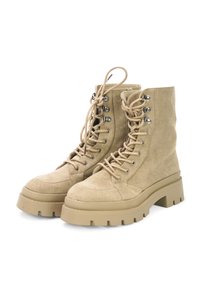 Beige suede ankle boots with a chunky rubber sole, round toe, and metal eyelets. Features prominent lacing and a cushioned shaft.
