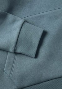 Sudadera de color azul claro con un tejido texturizado, detalle en los puños y costuras cosidas, que presenta un ajuste relajado y un material suave.