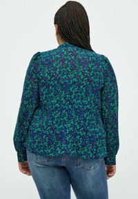 Blusa floreale con un motivo blu navy e verde, maniche a sbuffo e polsini con bottoni. Realizzata in tessuto leggero con una vestibilità comoda.