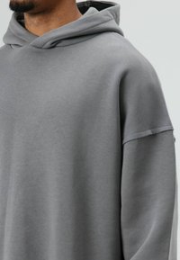 Grijze hoodie met een zachte textuur, losse pasvorm en korte mouwen. Heeft een grote capuchon en minimale naden, wat zorgt voor een strak ontwerp.